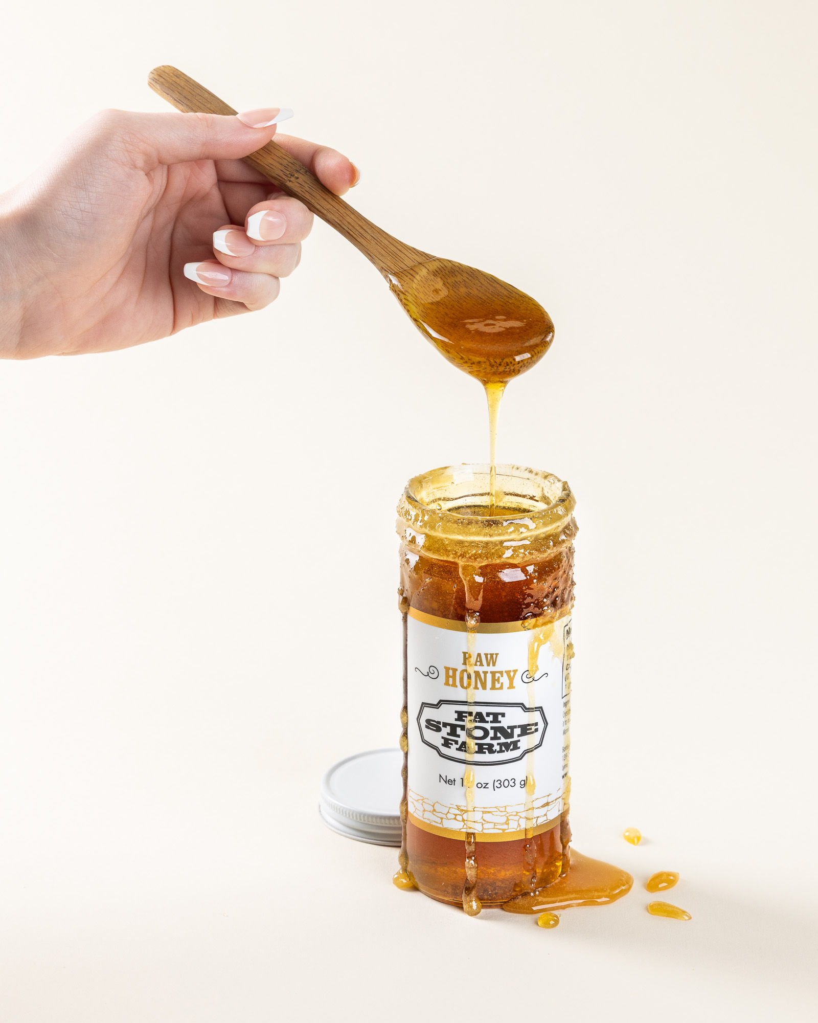 woman's hand holding wooden spoon dripping with honey into a jar by Fat Stone Farm honey